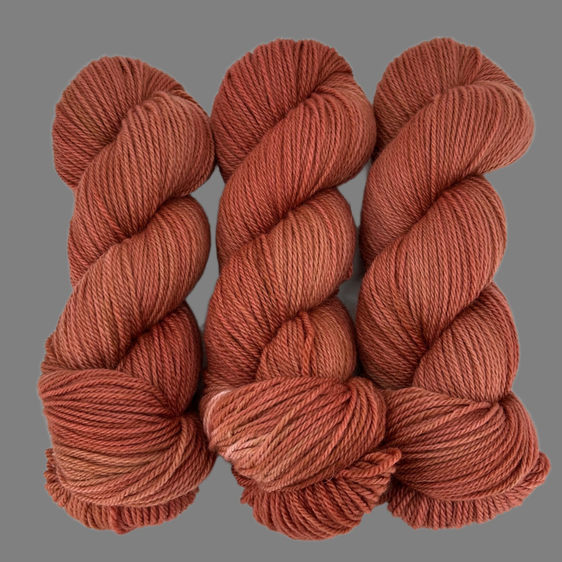 Three skeins of rusty red brown yarn on a gray  background