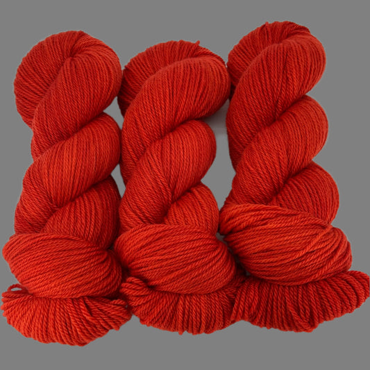 Three skeins of orange leaning  red yarn on a gray  background